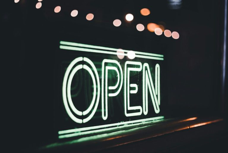 Neon-Schild in grün mit der Aufschrift "OPEN" vor unscharfem Hintergrund.