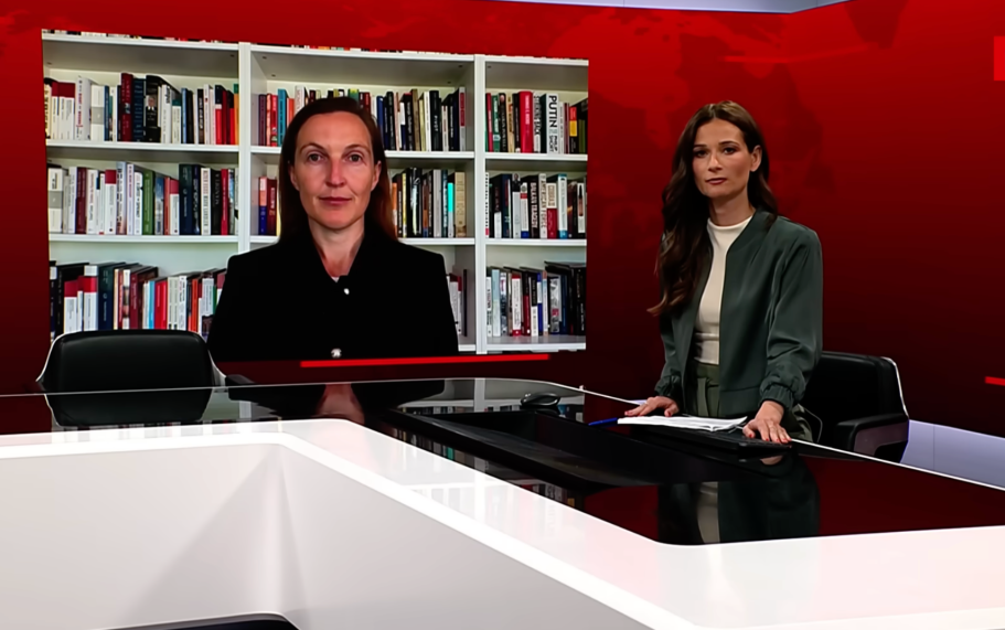 BR24 Interview Nachrichtenszene im Fernsehstudio mit US-Präsident Trump und Bundeskanzler Merz im Hintergrund.