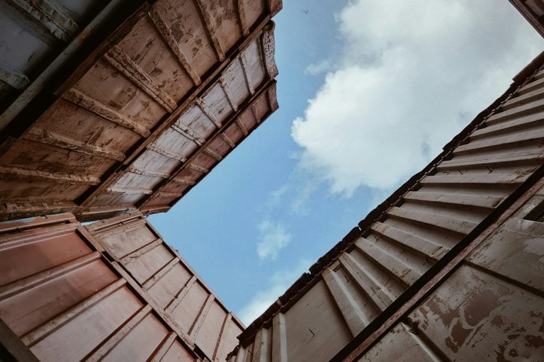 Blick nach oben zwischen Containern auf einen blauen Himmel mit Wolken.