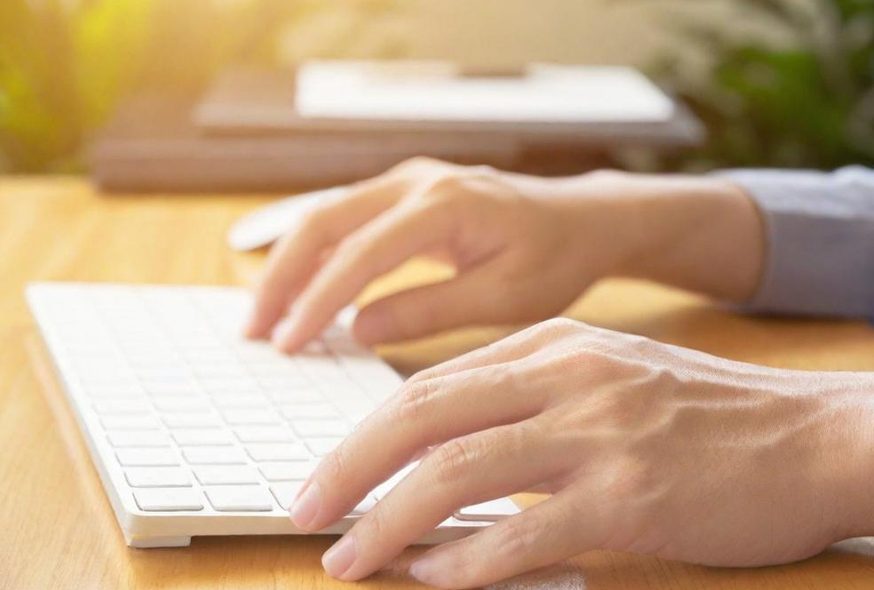 Meldung Zeitungsinterview Hände tippen auf einer weißen Tastatur auf einem Holztisch.