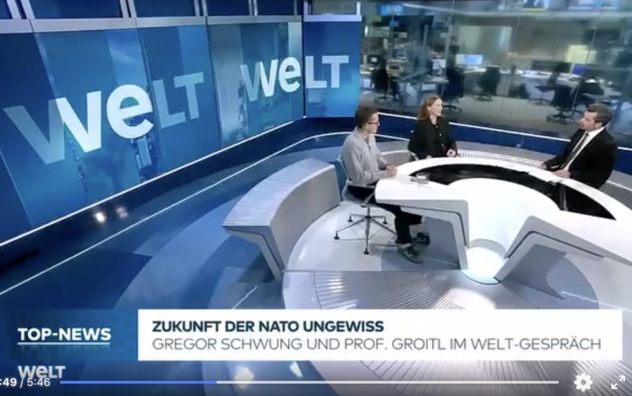 BR24 Interview Nachrichtenszene im Fernsehstudio mit US-Präsident Trump und Bundeskanzler Merz im Hintergrund.