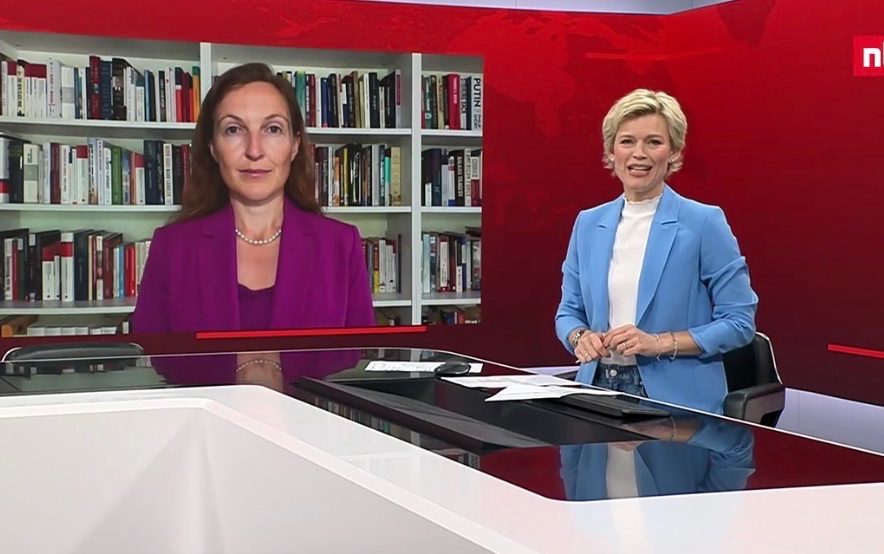 BR24 Interview Nachrichtenszene im Fernsehstudio mit US-Präsident Trump und Bundeskanzler Merz im Hintergrund.