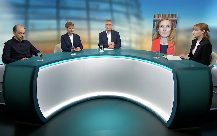 BR24 Interview Nachrichtenszene im Fernsehstudio mit US-Präsident Trump und Bundeskanzler Merz im Hintergrund.
