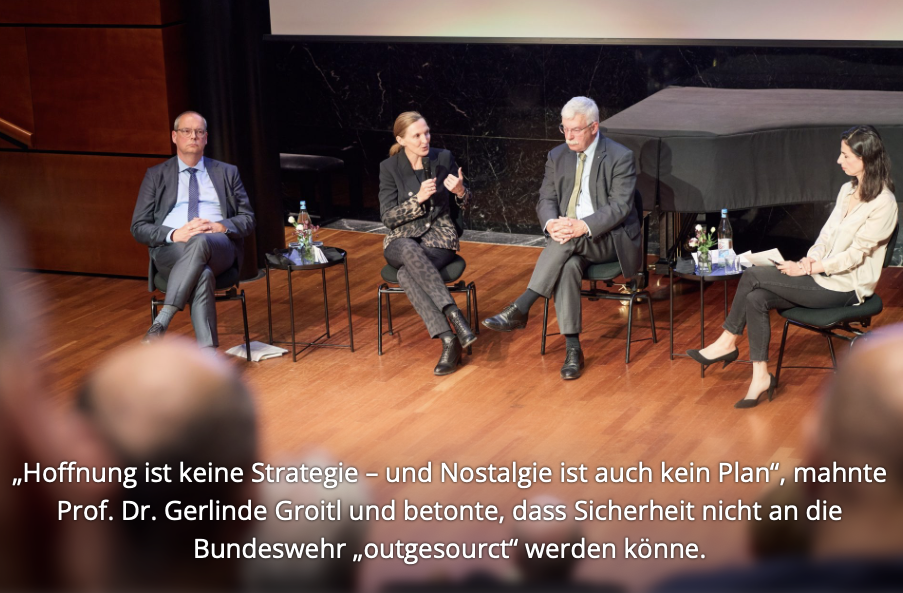Konferenz mit mehreren Sprechern an einem Tisch vor einer Logo-Wand.
