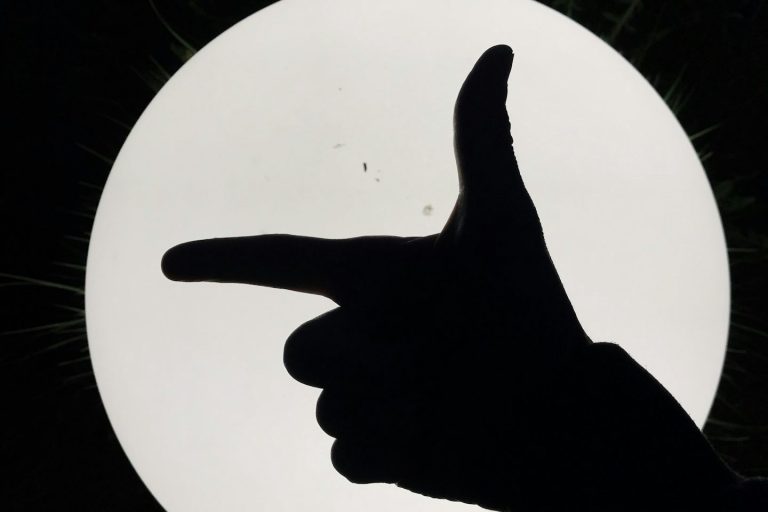 Silhouette einer Hand, die mit Finger eine Pistole vorm hellen Hintergrund formt.