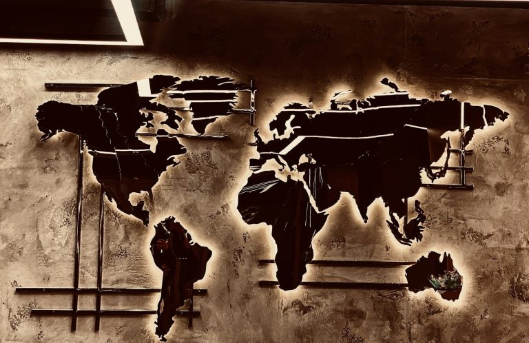 Weltkarte aus Metall, künstlerisch an der Wand angebracht, mit beleuchteten Konturen.