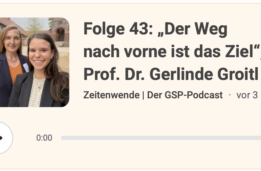 Konferenz mit mehreren Sprechern an einem Tisch vor einer Logo-Wand.