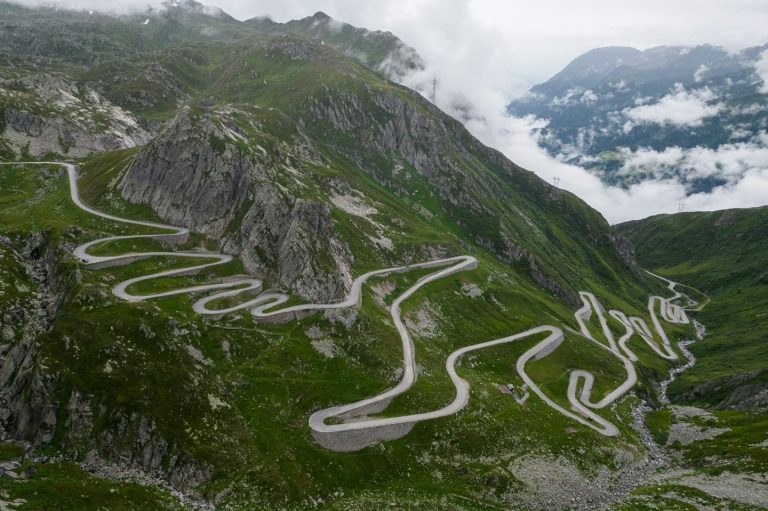Symbolbild Herausforderung Kurvige Serpentinenstraße durch grüne Berge mit Wolkenhimmel im Hintergrund.