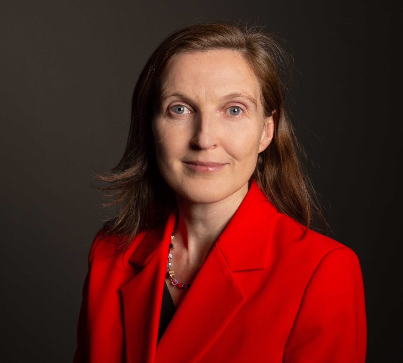 Gerlinde Groitl trägt einen roten Blazer und schaut in die Kamera.