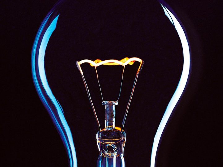 Glühbirne mit leuchtendem Glühdraht vor dunklem Hintergrund.