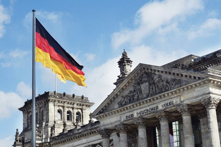 Deutsche Flagge weht vor dem Reichstag in Berlin unter blauem Himmel.