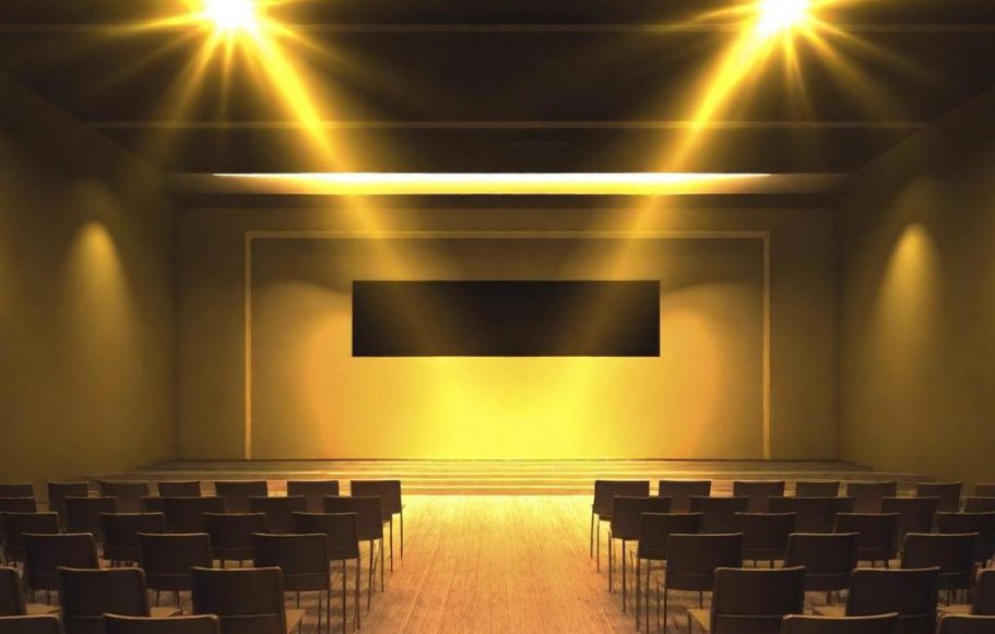 Symbolbild Veranstaltungssaal Leerer Raum mit Stuhlreihen und einer Leinwand, beleuchtet von scheinen Lichtern.